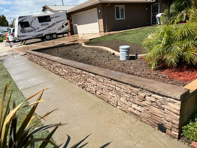 Stacked stone retaining wall with concrete walkway and landscape edging