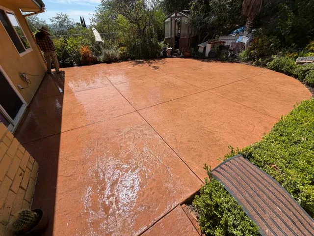 Finished concrete patio with control joints, wet surface showing orange-tinted concrete