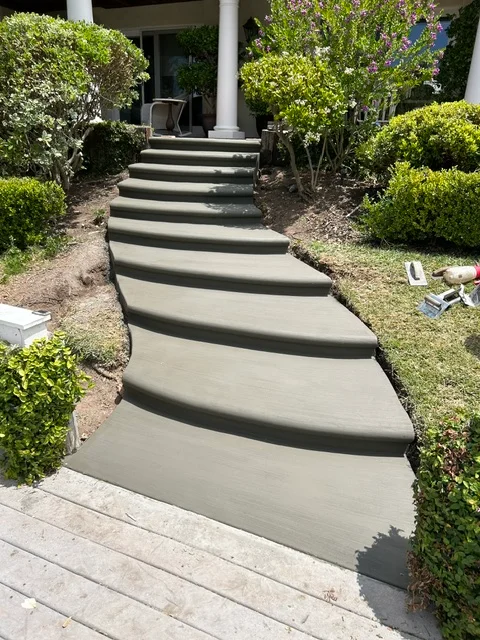 Curved concrete walkway with integrated steps and dark scoring lines, flanked by manicured boxwood hedges