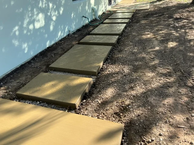 Concrete stepping stones installed in gravel base along building foundation