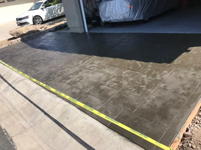 Dark gray stamped concrete driveway with linear tile pattern and control joints