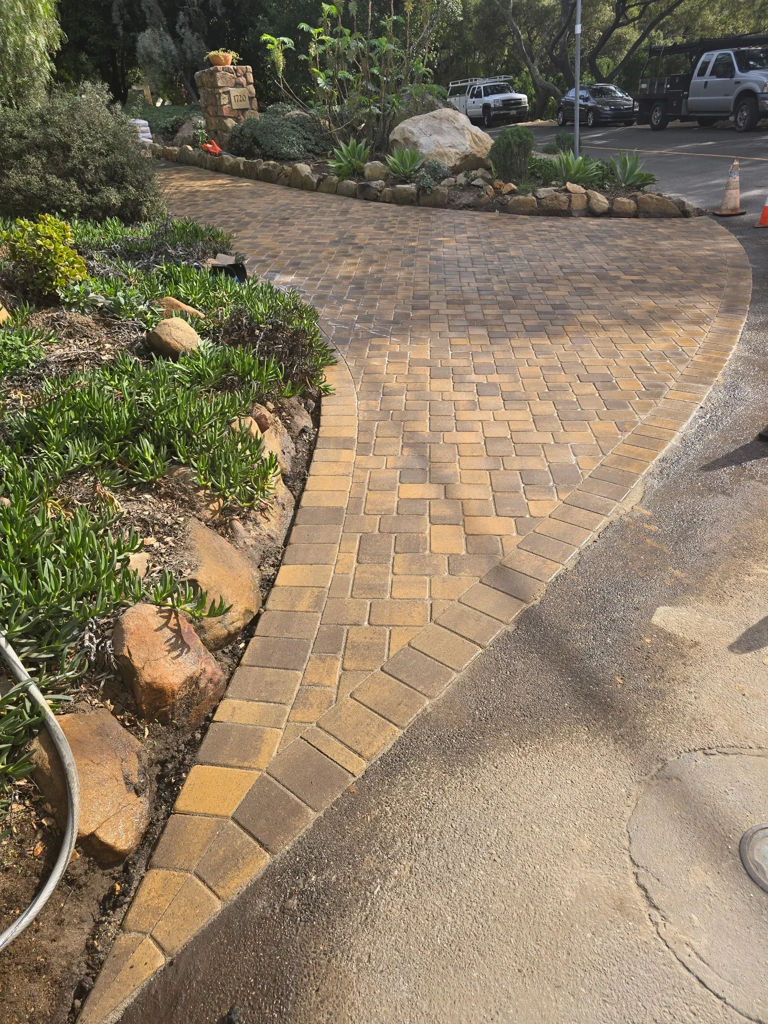 Curved paver driveway with herringbone pattern, boulders, and landscape edging