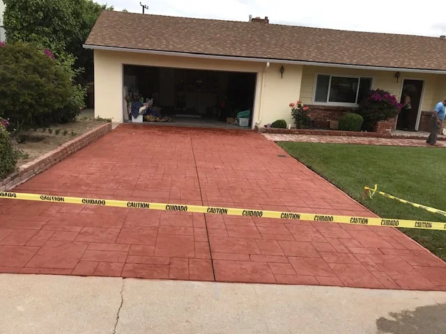 Newly poured red concrete driveway with control joints and finished edges