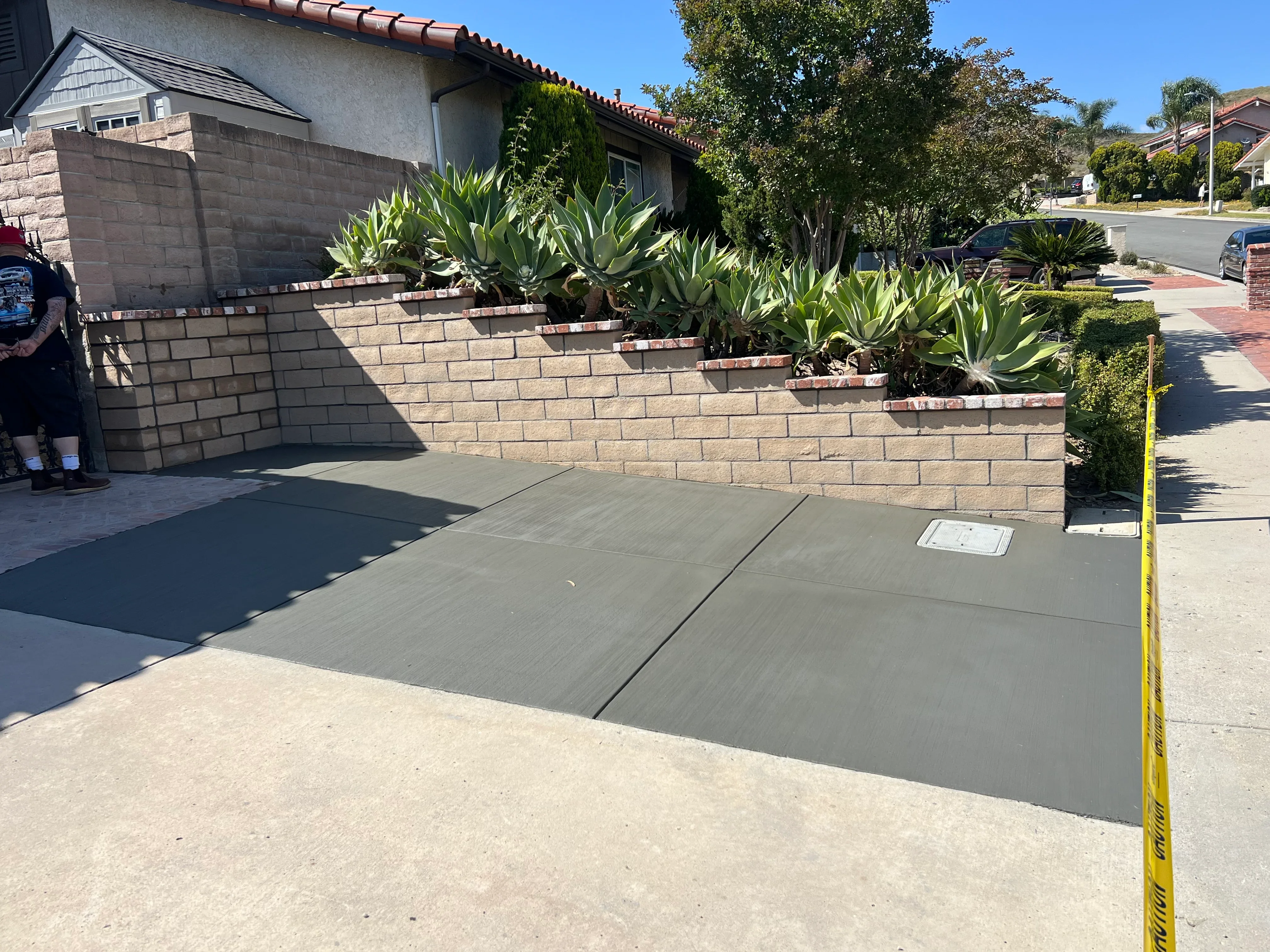 Gray concrete driveway with control joints installed in front of residential home with stone retaining wall