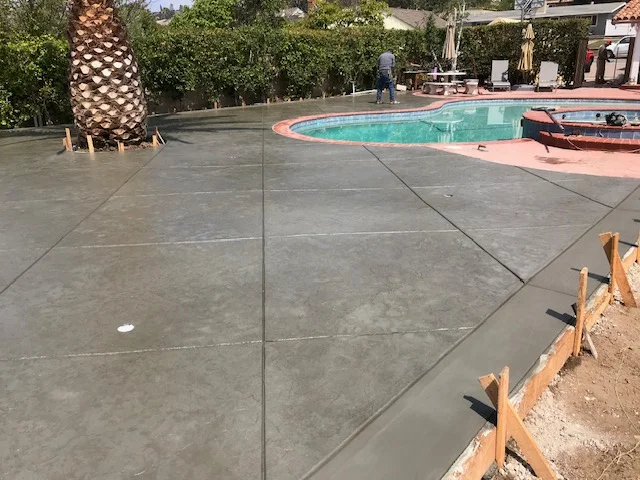 Large concrete patio with control joints, pool deck area with palm tree and pool visible