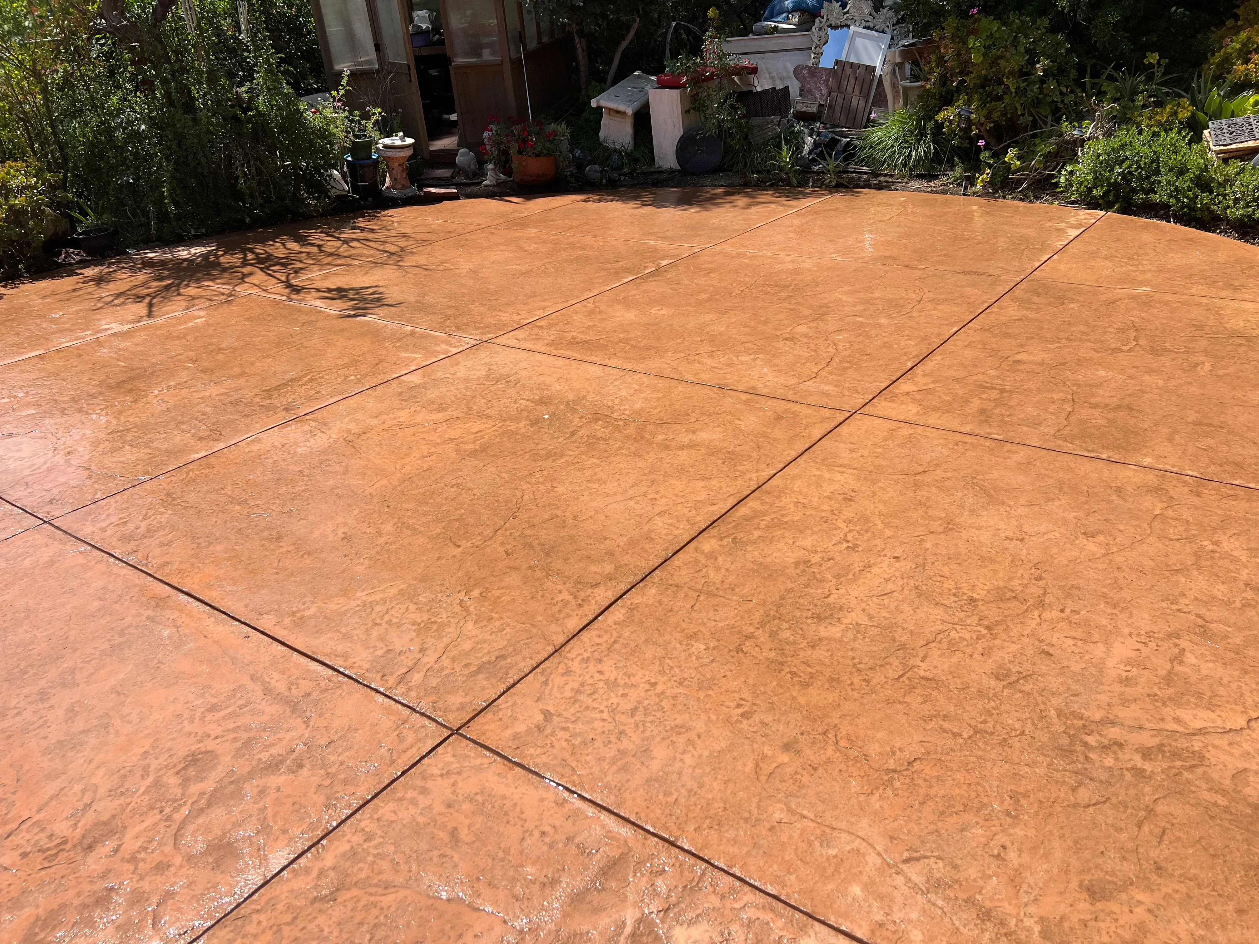 Stamped concrete patio with terracotta finish and control joints, bordered by landscaping