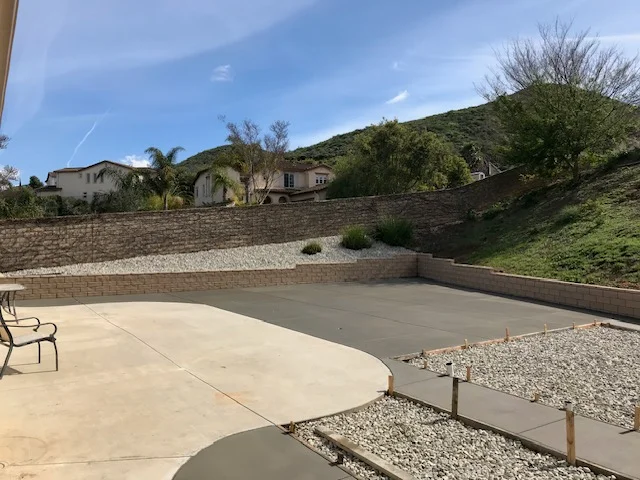 Concrete patio with control joints, brick retaining walls, and river rock landscaping on hillside