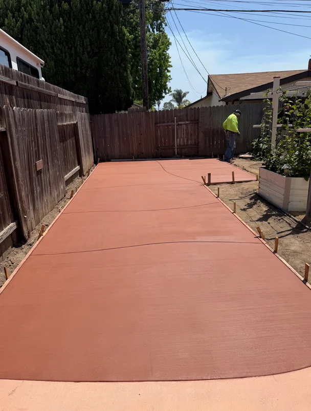 Newly poured terracotta concrete driveway with control joints and wooden forms in residential backyard