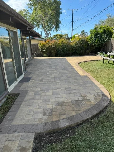 Gray paver patio with curved design and black edging bordering lawn area