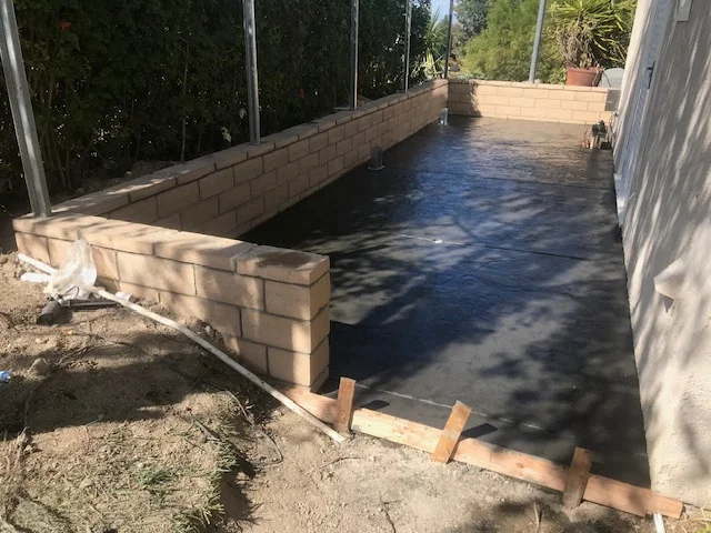 Newly poured concrete pool deck with cinder block walls and wooden bracing during curing