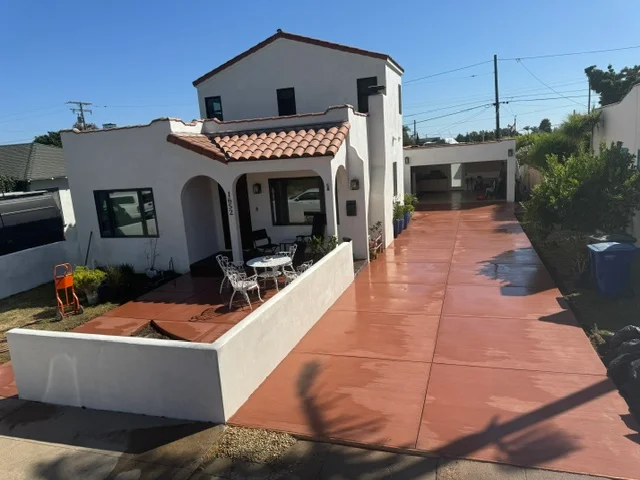 Red concrete patio with decorative finish in front of Spanish Colonial home with white stucco and tile roof