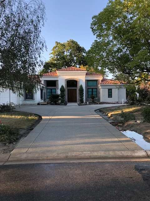 Newly poured concrete driveway leading to white stucco home with clay tile roof