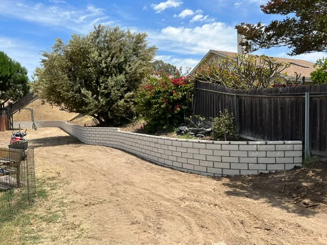 Curved gray concrete block retaining wall with proper grading and landscape integration