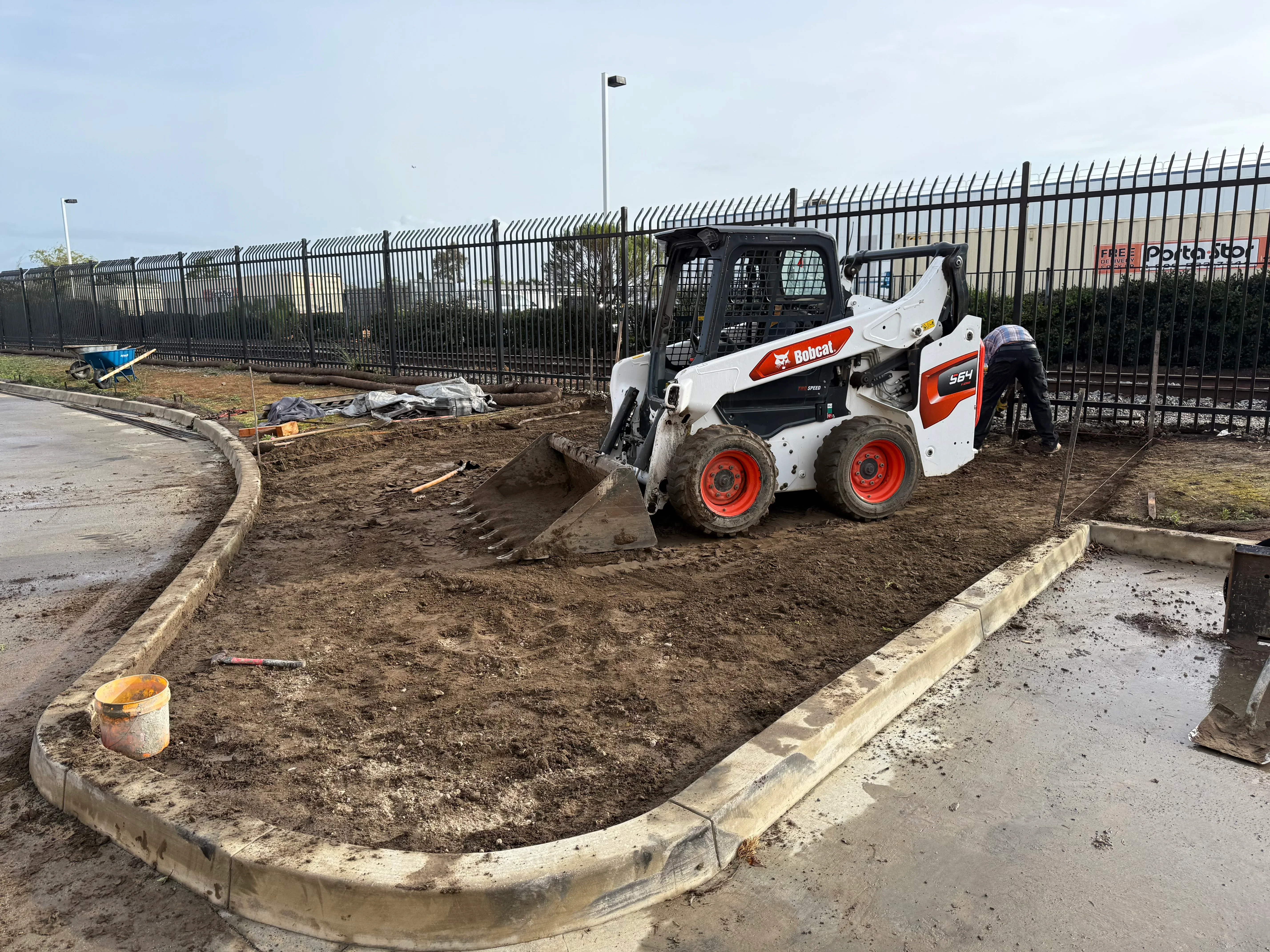 Bobcat skid steer grading soil within concrete curb forms on prepared site