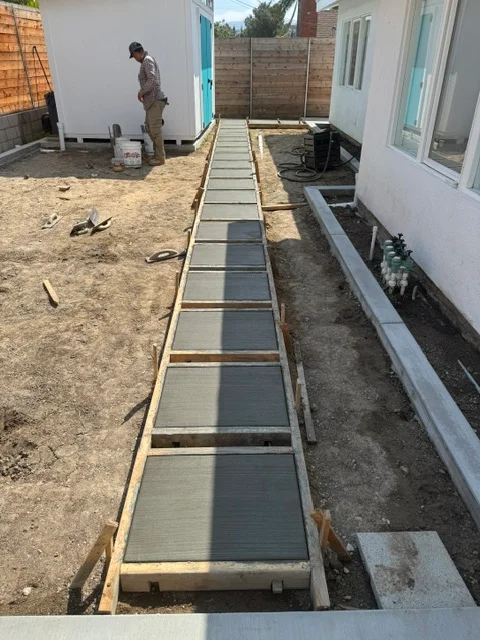 Concrete walkway with pavers and metal drainage edging along residential foundation