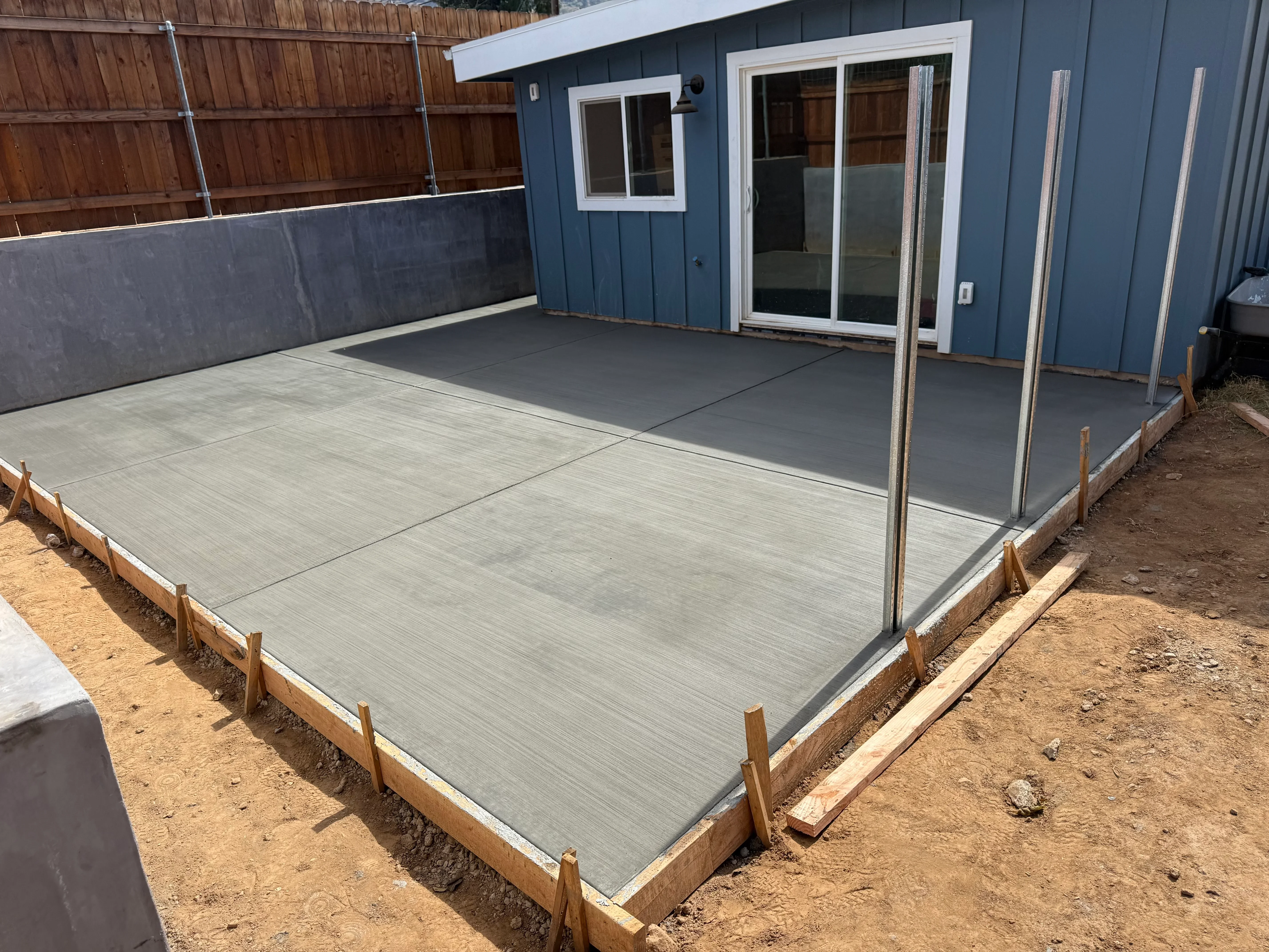 Gray concrete patio with control joints and wooden forms, adjacent to blue residential building