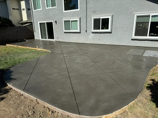 Dark gray concrete patio with control joints and curved edges adjacent to residential home