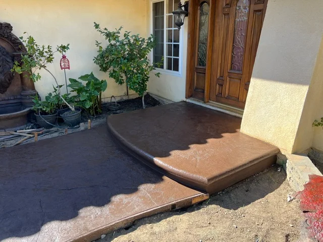 Newly poured concrete patio with stepped transition and dark finish, adjacent to residential entry door