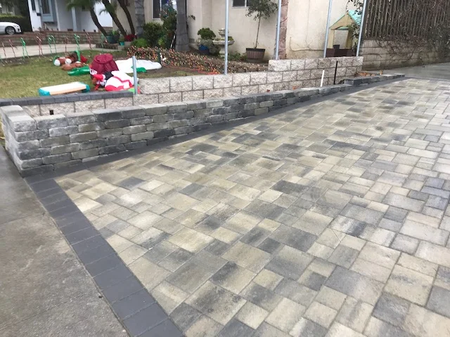 Gray and tan concrete paver patio with stacked stone retaining wall and landscape edging