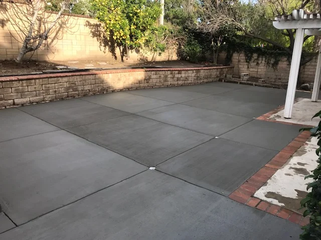 Gray concrete patio with control joints and red brick border edging
