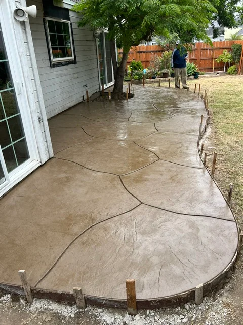 Curved concrete patio with decorative scoring patterns and curved borders next to residential home