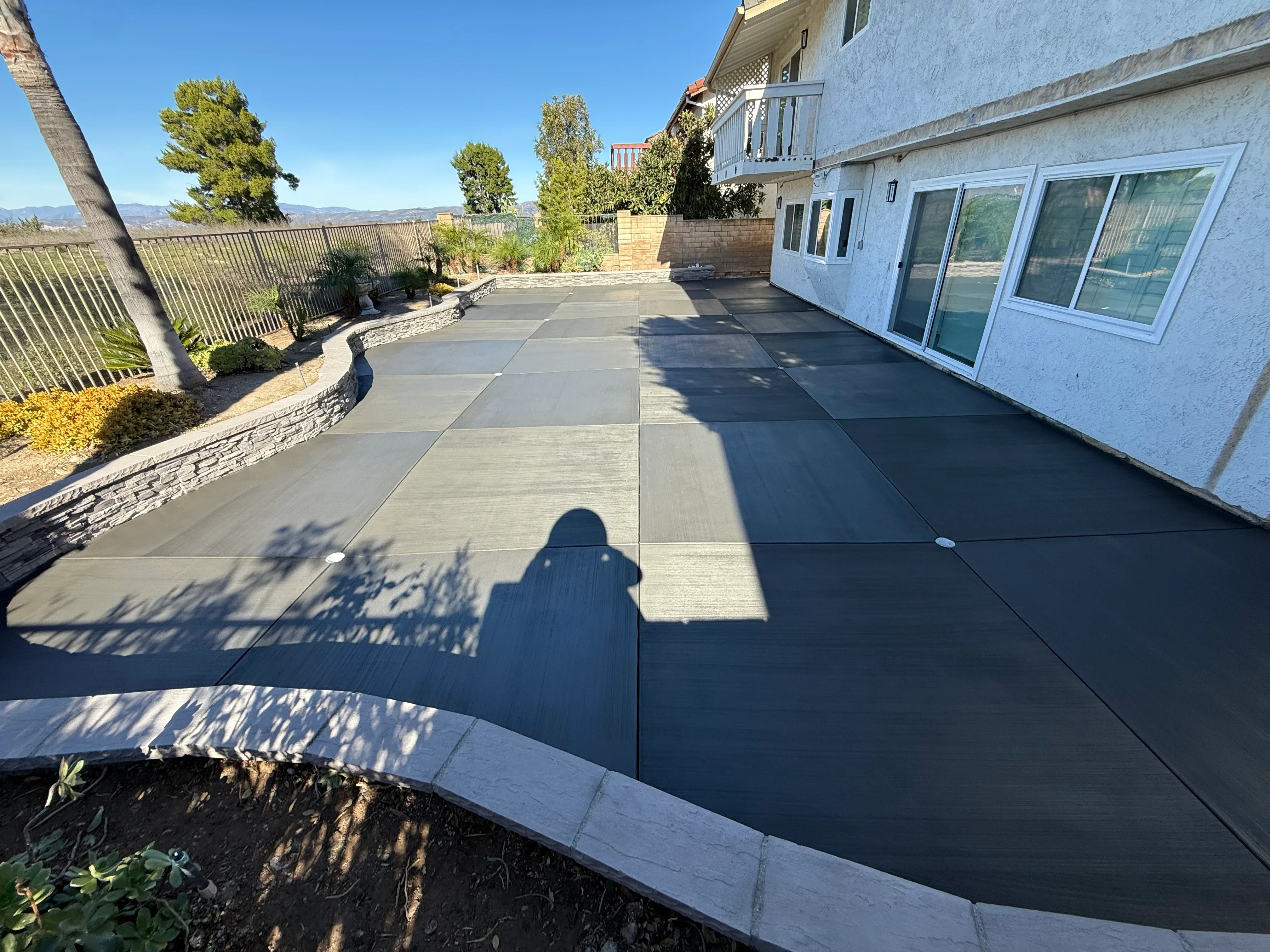 Finished concrete patio with control joints, curved stone veneer edging, and two-tone concrete finish
