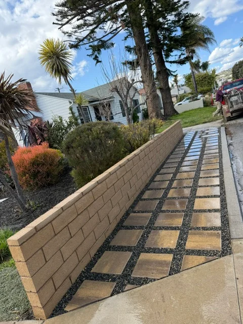 Decorative concrete pathway with geometric pattern and tan concrete block retaining wall