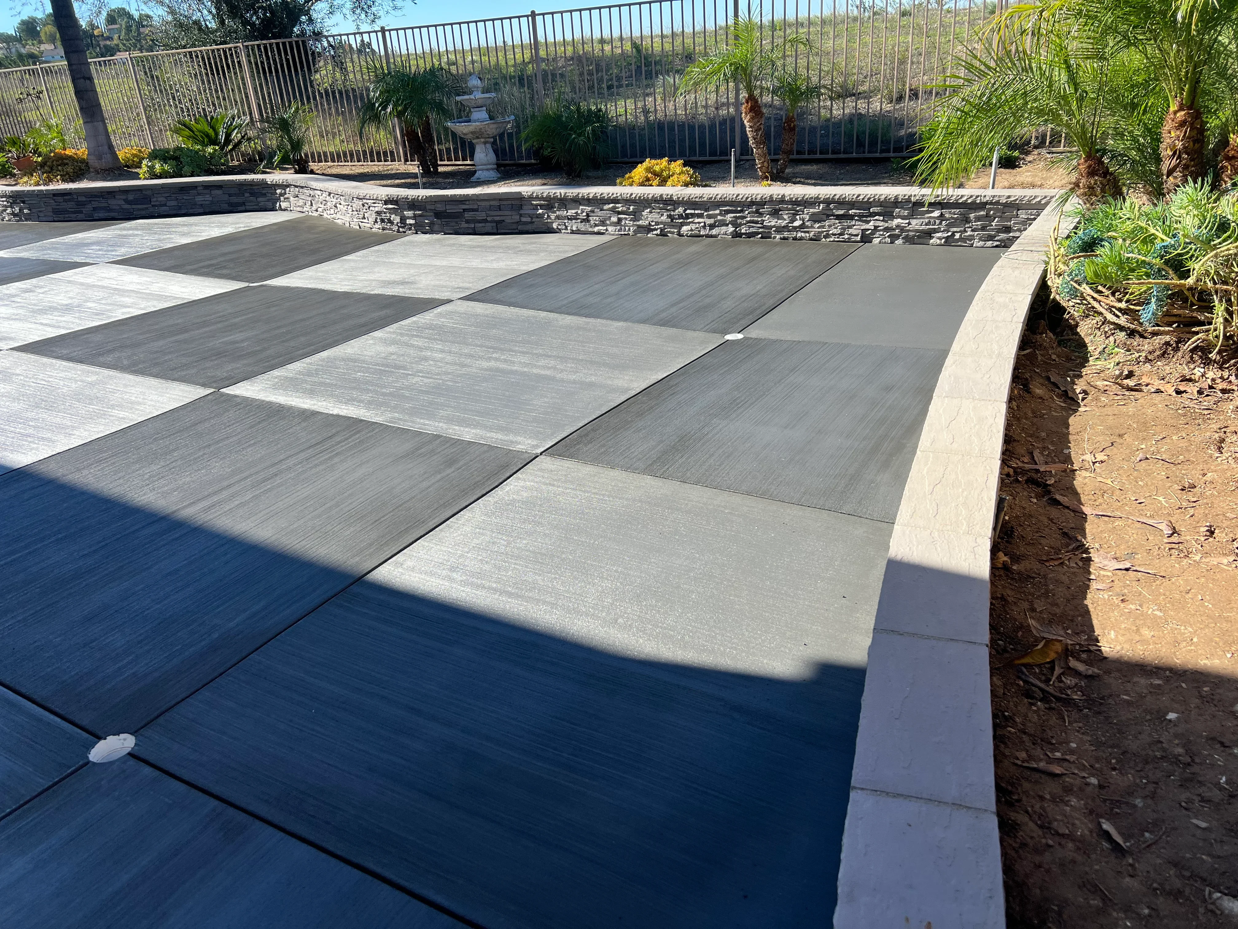 Geometric concrete patio with alternating gray tones, stone retaining wall, and concrete edging