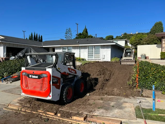 Bobcat skid-steer loader grading soil for residential concrete foundation work