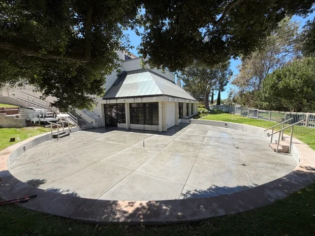 Large concrete patio with curved edges and control joints, modern home with metal roof in background